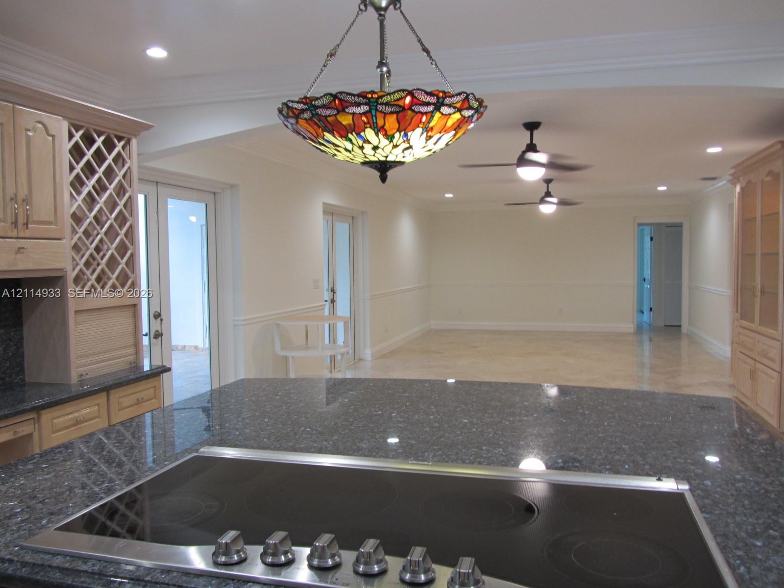 Kitchen featuring dark stone countertops, a glass-top cooktop, light wood cabinetry with built-in wine storage, recessed lighting, and a stained glass pendant fixture