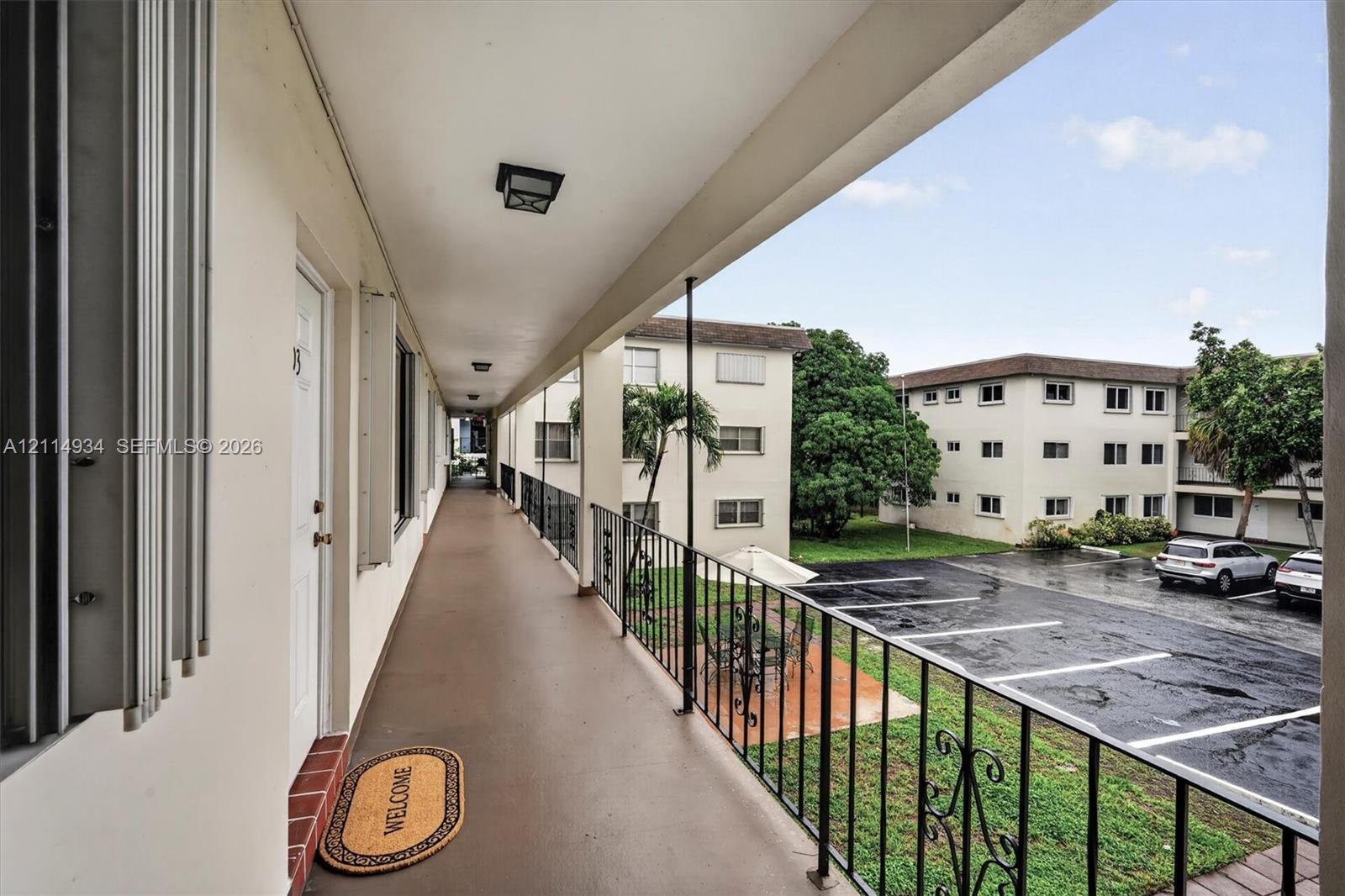 Covered exterior walkway featuring a smooth concrete surface, flush-mount ceiling lighting, and decorative black metal railings