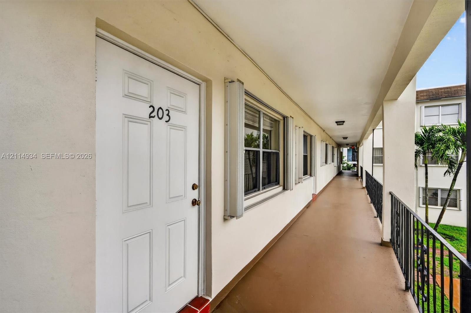 Covered exterior walkway featuring painted concrete flooring, recessed lighting, and black metal railings