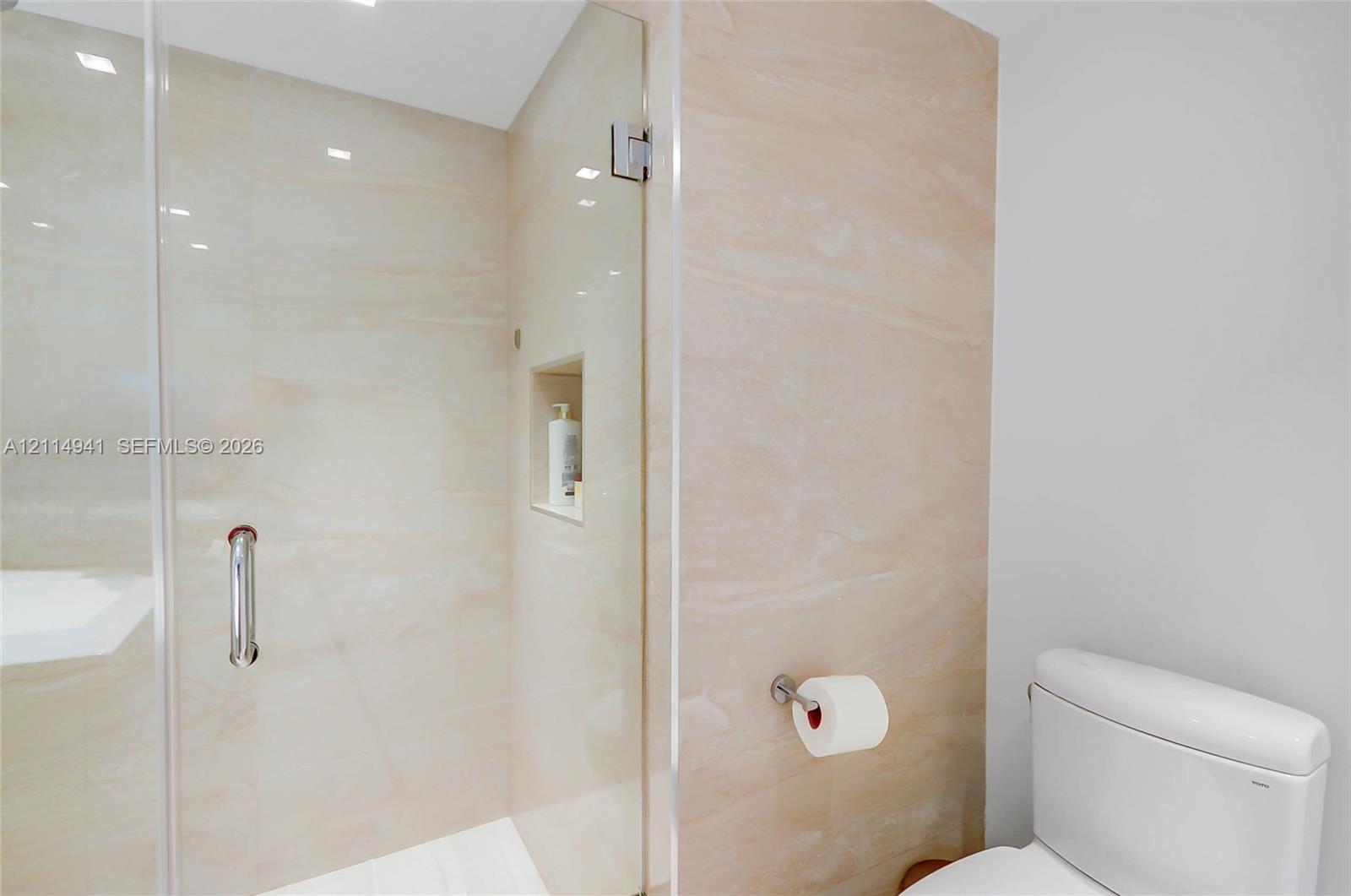 Walk-in shower featuring large-format stone-look tile, frameless glass door, polished chrome hardware, and built-in recessed wall niche