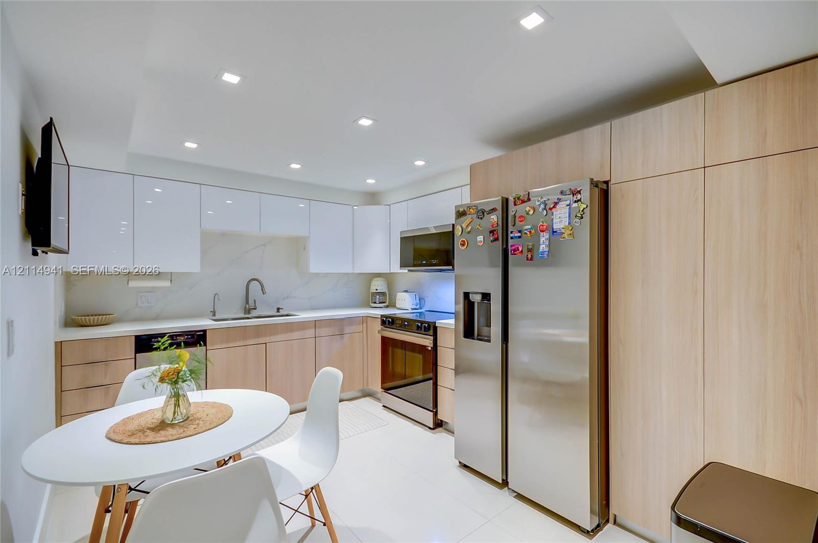 Kitchen featuring high-gloss upper cabinetry, wood-finish lower cabinetry, stone-style backsplash, integrated stainless steel appliances, and recessed lighting