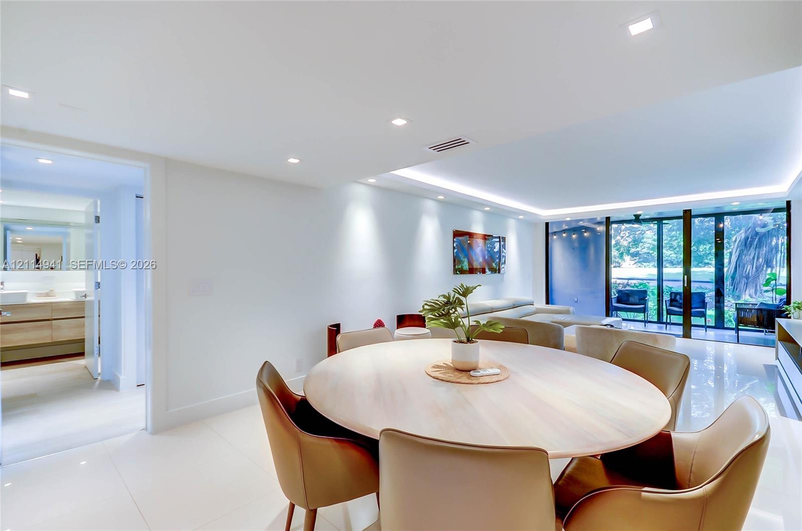 Open-concept interior featuring large-format tile flooring, recessed ceiling lighting, indirect cove lighting, and floor-to-ceiling sliding glass doors Open-concept interior featuring large-format tile flooring, recessed ceiling lighting, indirect cove lighting, and floor-to-ceiling sliding glass doors