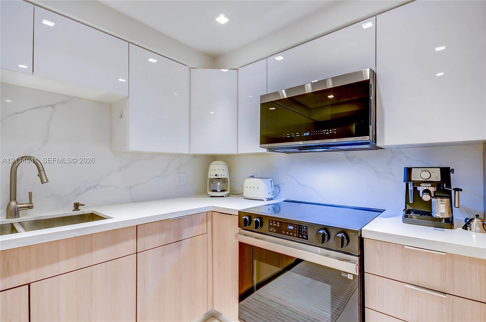 Modern kitchen featuring high-gloss white upper cabinetry, wood-finish lower cabinetry, solid-surface countertops, stone-patterned backsplash, and integrated stainless steel appliances
