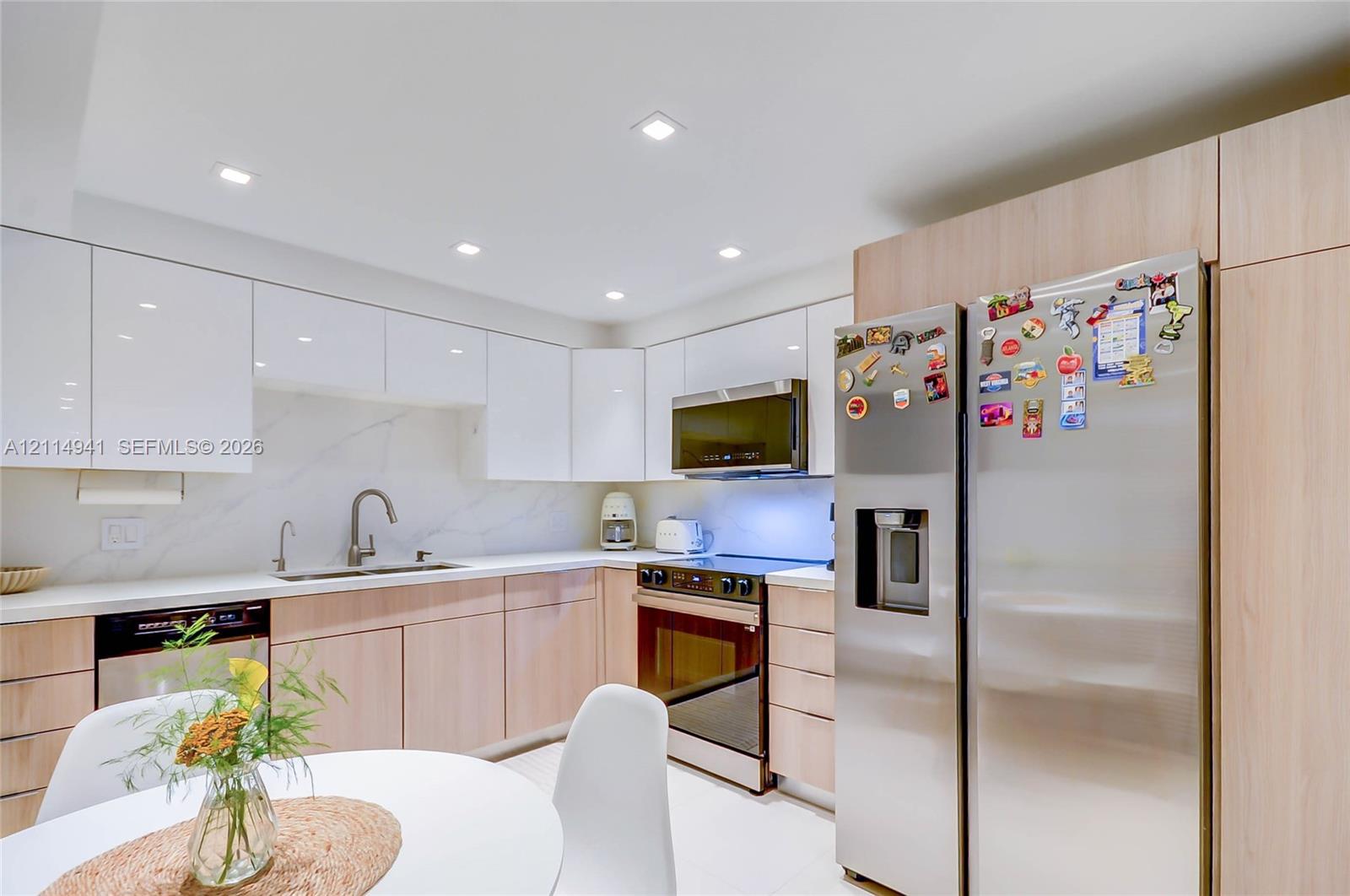 Kitchen featuring high-gloss white upper cabinetry, wood-finish base cabinetry, stone-style backsplash, integrated stainless steel appliances, and recessed ceiling lighting