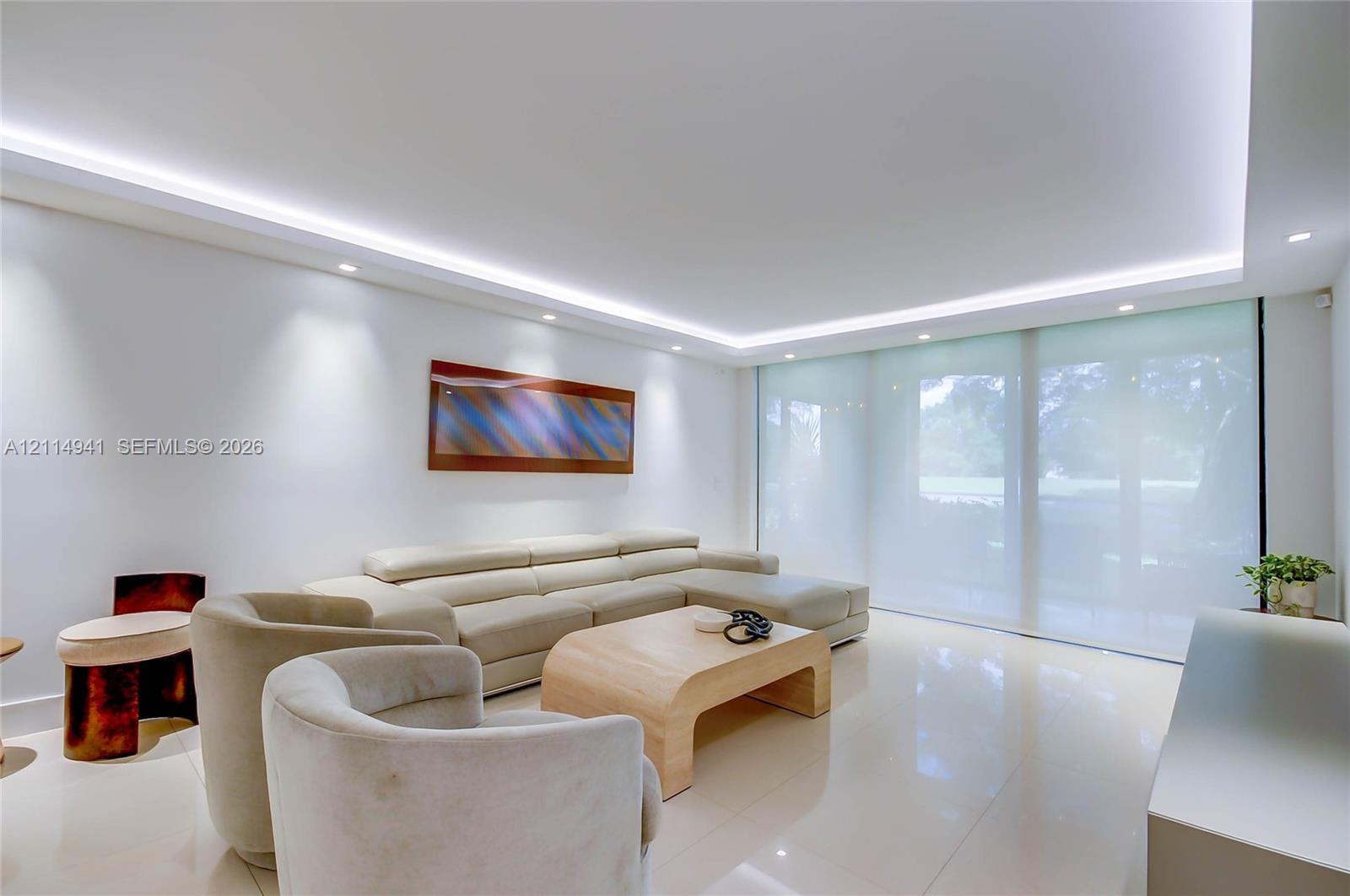 Expansive living space featuring polished light-toned tile flooring, recessed cove lighting, and floor-to-ceiling sliding glass doors with integrated roller shades Expansive living space featuring polished light-toned tile flooring, recessed cove lighting, and floor-to-ceiling sliding glass doors with integrated roller shades