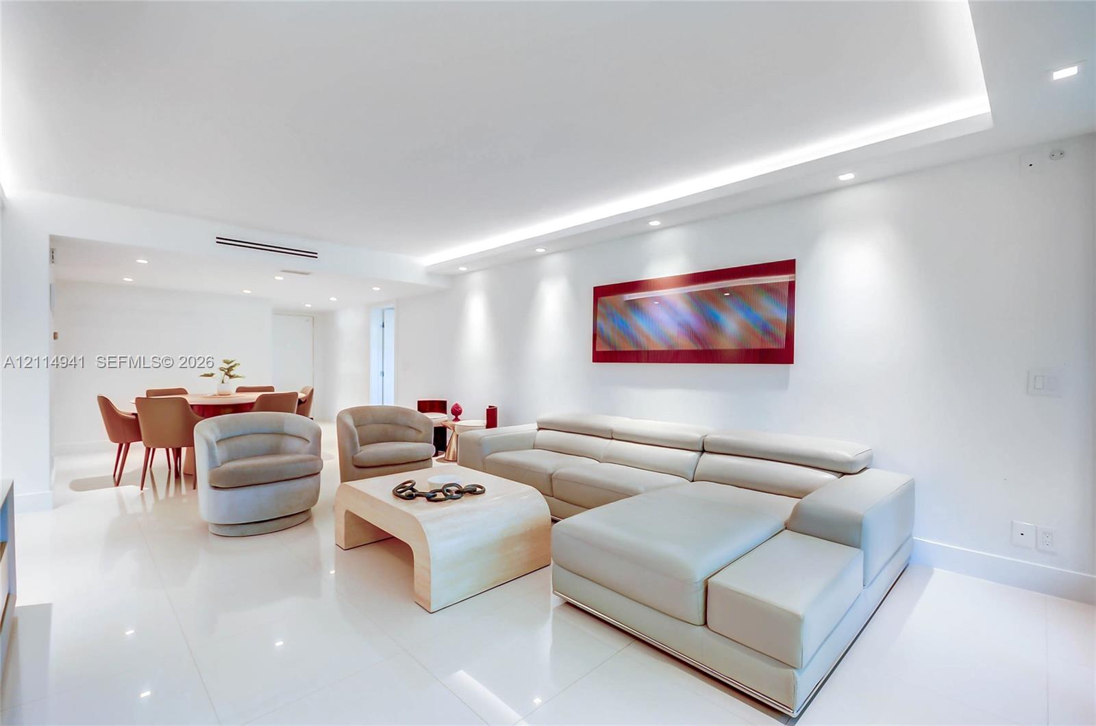 Open-concept living space featuring high-gloss tile flooring, recessed lighting, cove ceiling detail with integrated ambient lighting, and neutral wall finishes Open-concept living space featuring high-gloss tile flooring, recessed lighting, cove ceiling detail with integrated ambient lighting, and neutral wall finishes