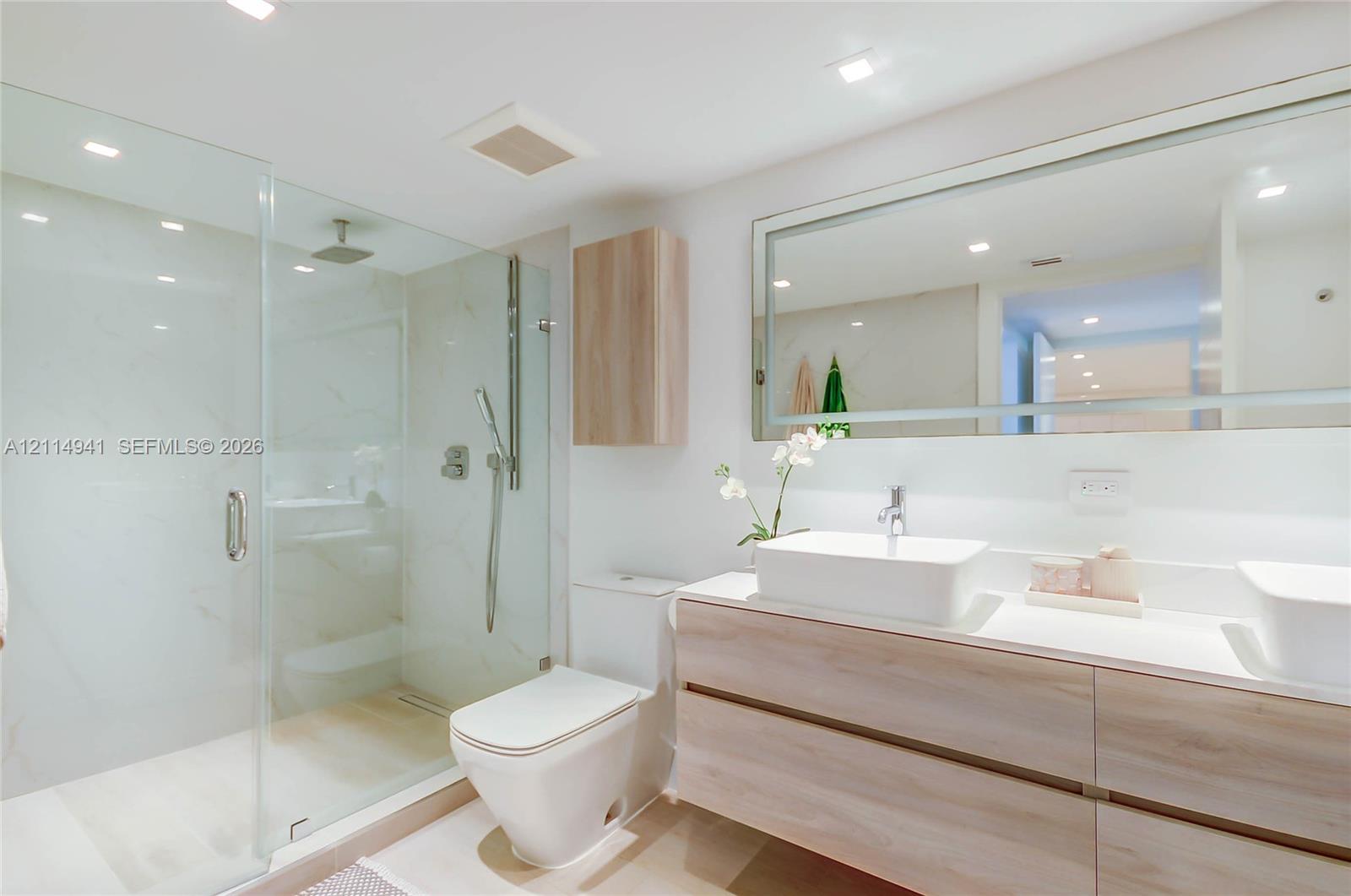 Bathroom featuring a floating wood-finish double vanity, dual vessel sinks, glass-enclosed shower with tiled walls, and an expansive wall-mounted mirror