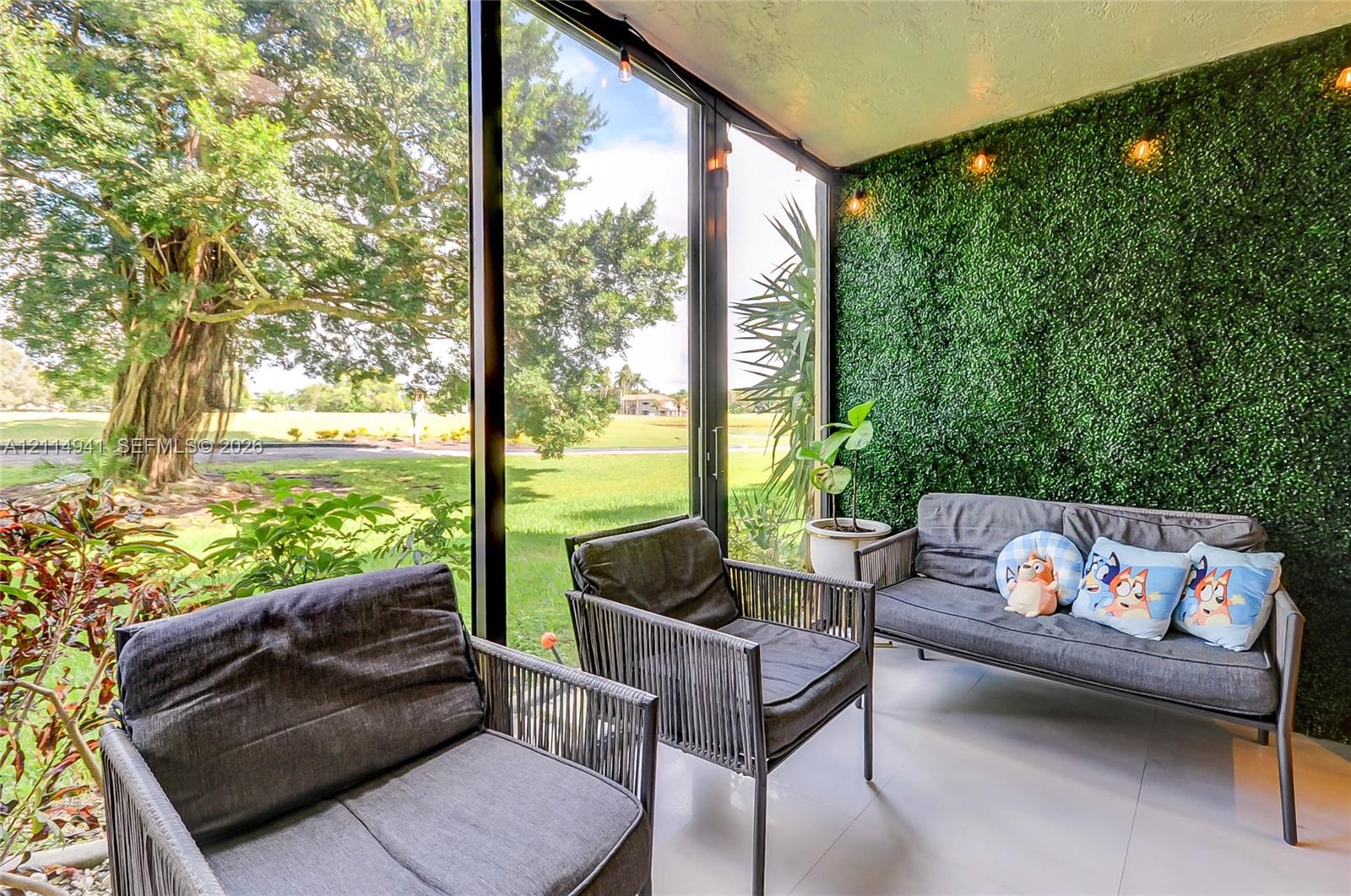 Enclosed porch featuring floor-to-ceiling glass paneling, tile flooring, and a decorative artificial hedge wall with integrated overhead lighting