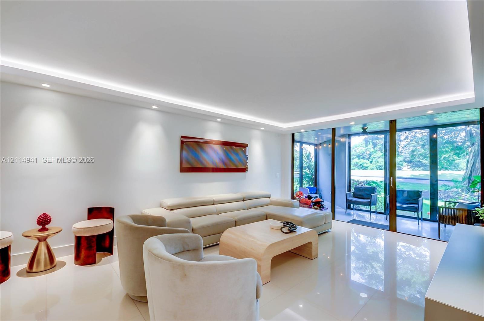Living space featuring light-toned flooring, recessed ceiling lighting with perimeter cove illumination, and floor-to-ceiling glass panel sliding doors Living space featuring light-toned flooring, recessed ceiling lighting with perimeter cove illumination, and floor-to-ceiling glass panel sliding doors