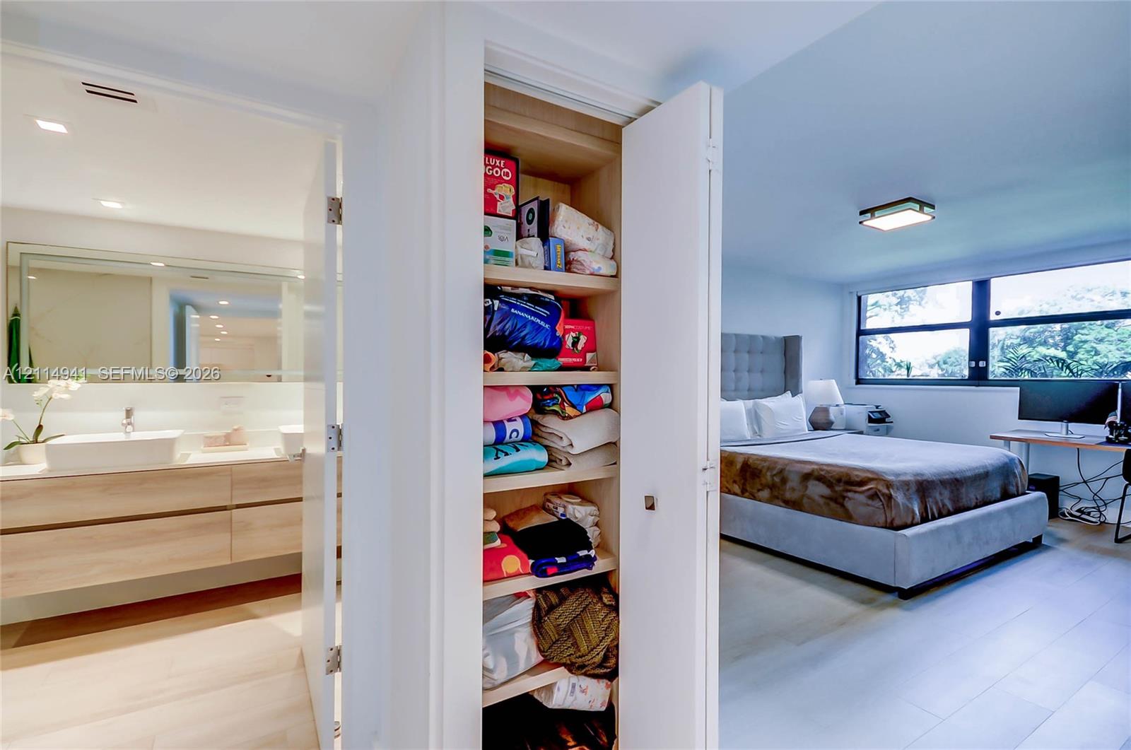 Built-in floor-to-ceiling storage cabinetry with adjustable shelving, light wood-finish floating vanity with dual rectangular vessel sinks, expansive vanity mirror, and large-format window panels