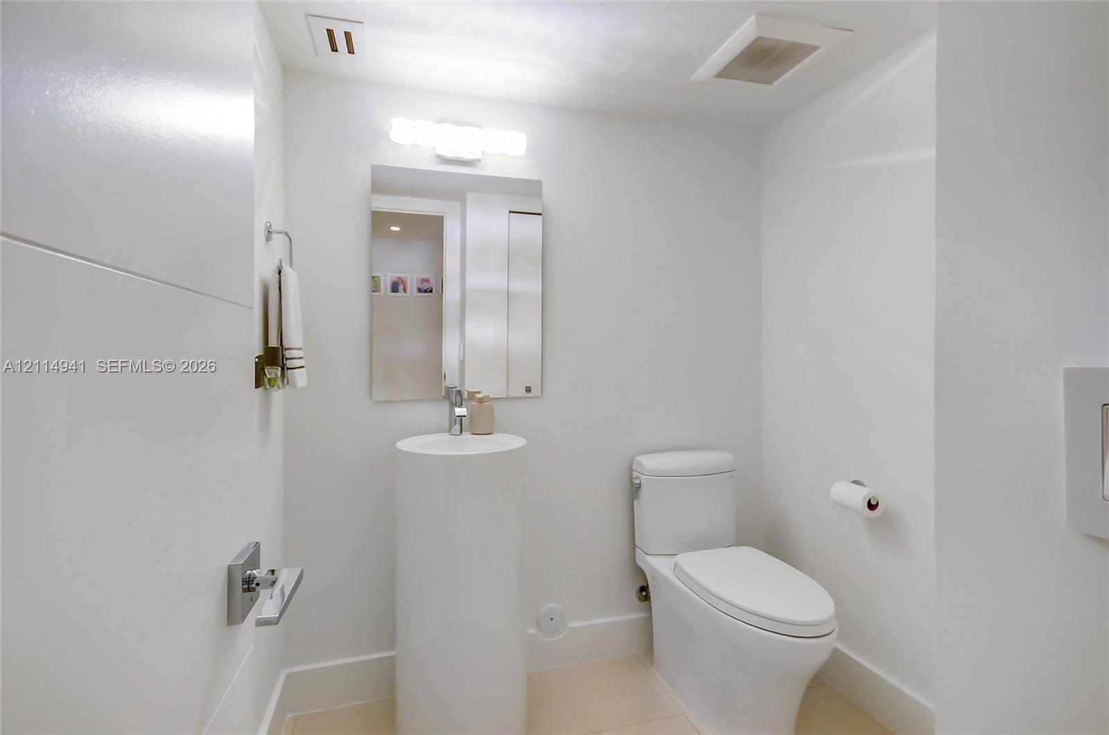 Cylindrical pedestal sink, rectangular wall-mounted mirror, chrome single-handle faucet, and white high-profile toilet