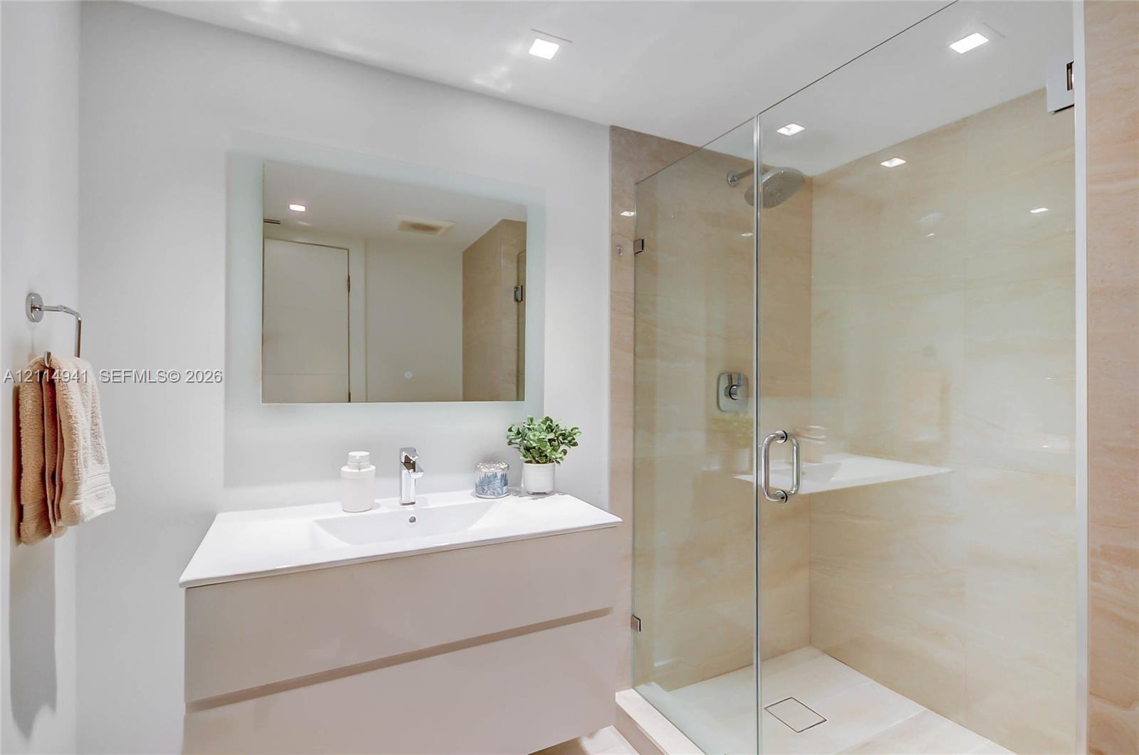 Floating vanity with an integrated sink, frameless glass-enclosed shower, stone-surround shower wall, recessed lighting, and a wall-mounted mirror