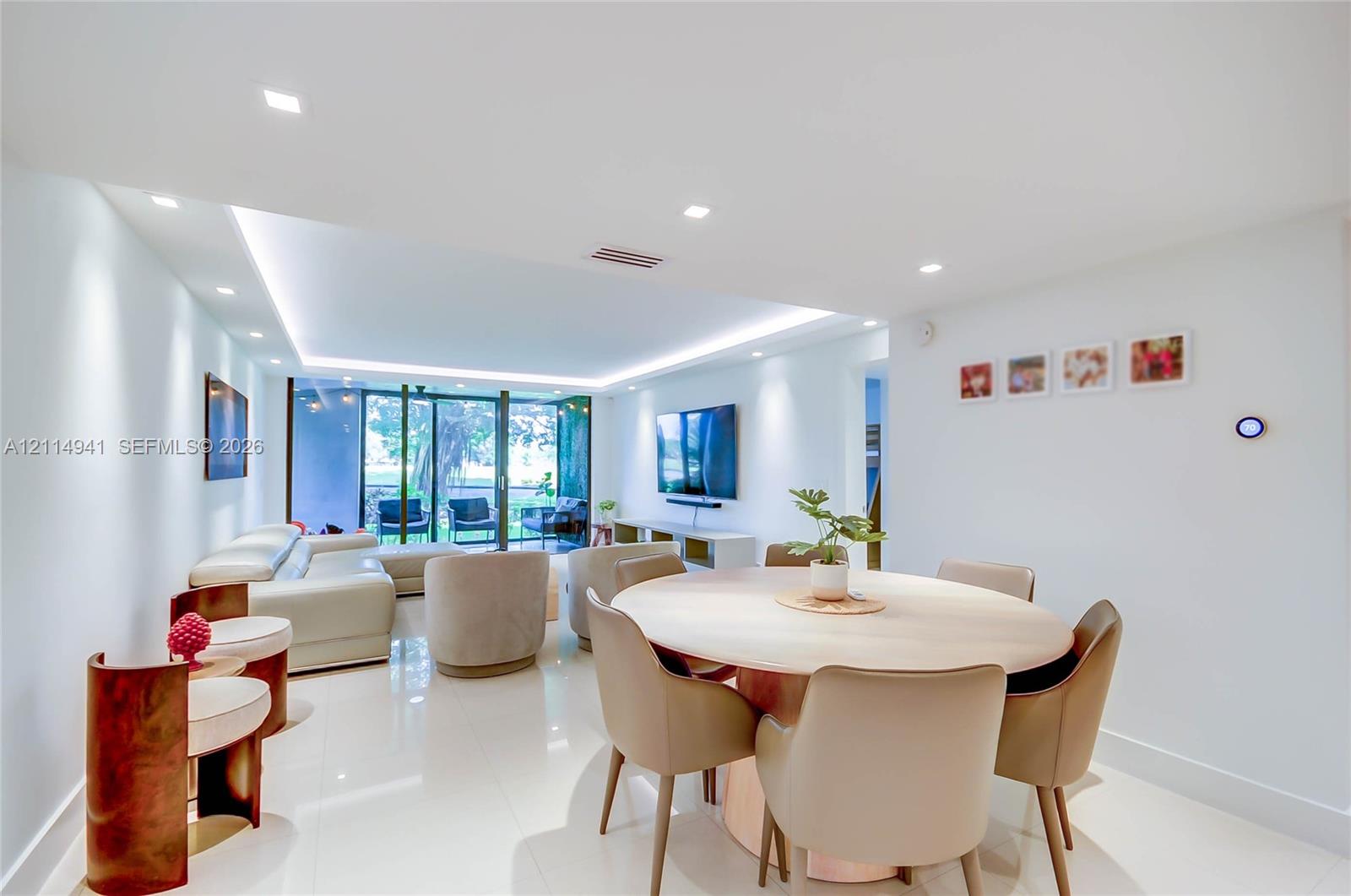Open-concept living space featuring high-gloss tile flooring, recessed lighting, ceiling tray with perimeter cove lighting, and floor-to-ceiling glass panel sliding doors Open-concept living space featuring high-gloss tile flooring, recessed lighting, ceiling tray with perimeter cove lighting, and floor-to-ceiling glass panel sliding doors