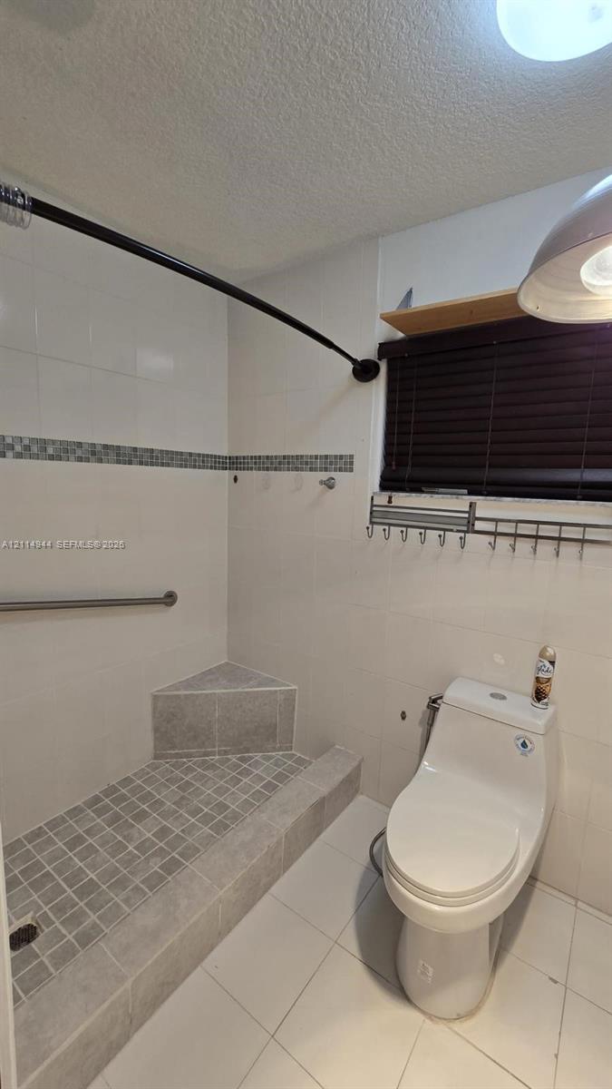 Walk-in shower featuring a built-in corner bench, mosaic tile flooring, decorative tile inlay, and white wall tiling with a stainless steel grab bar