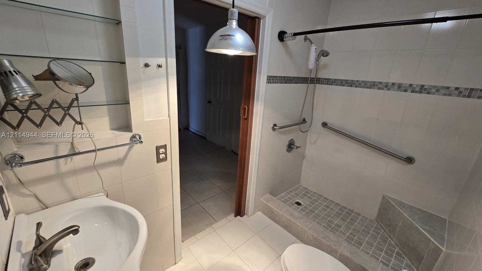 Bathroom featuring tiled flooring and walls, a step-in shower with integrated corner seating, wall-mounted metal grab bars, and a pendant-style light fixture