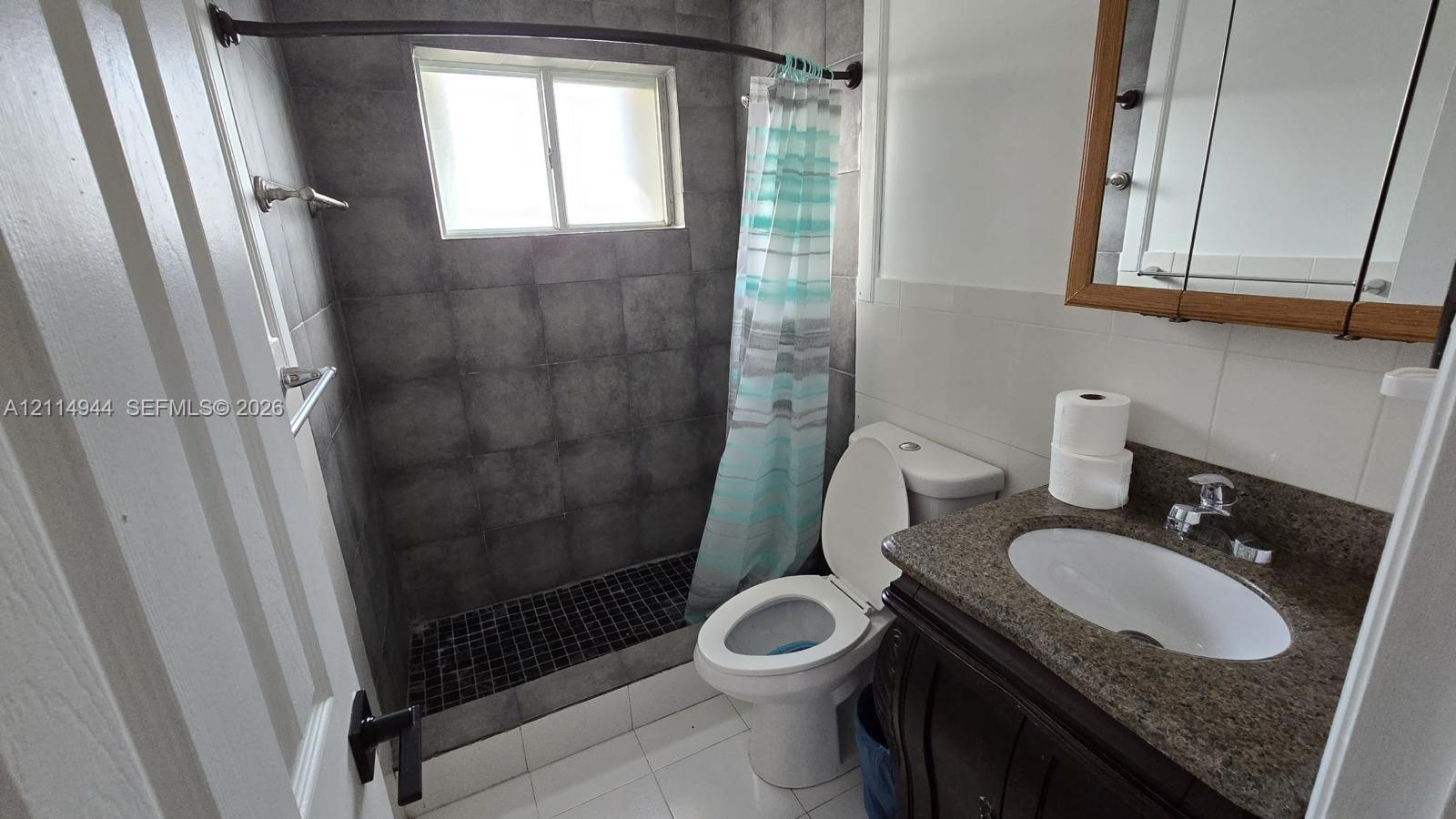 Bathroom featuring a vanity with an integrated basin, stone-composite countertop, full-height wall tiling within the shower enclosure, mosaic-tile shower flooring, and built-in medicine cabinet
