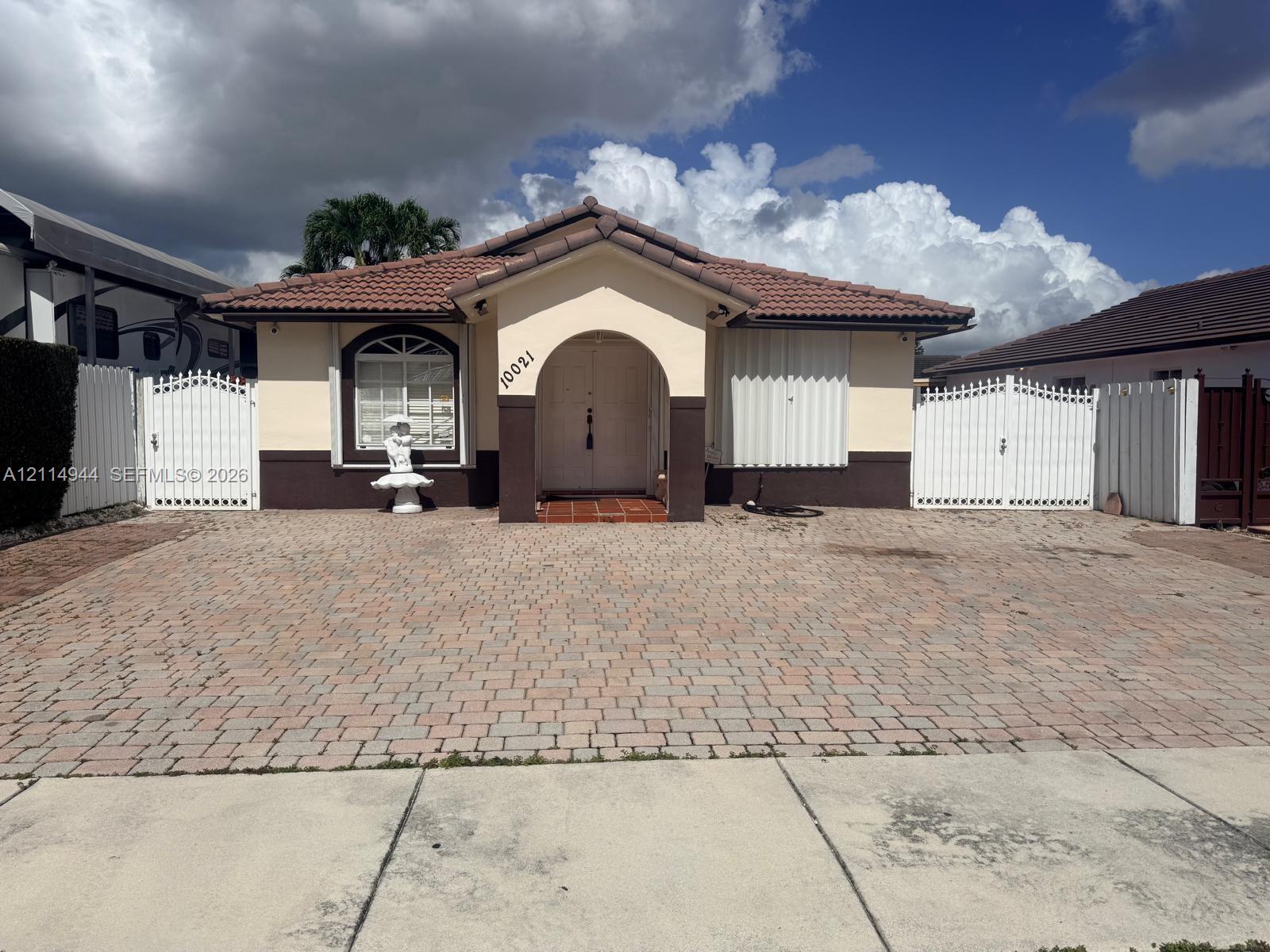 Single-story exterior featuring a tile roof, arched entryway, paved driveway, and decorative white privacy gates