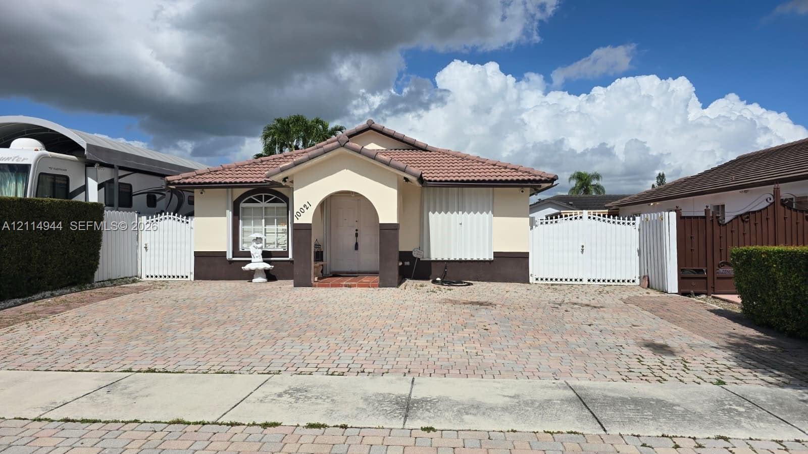 Single-story exterior featuring a tile roof, arched entryway, paved driveway, and dual white gate enclosures