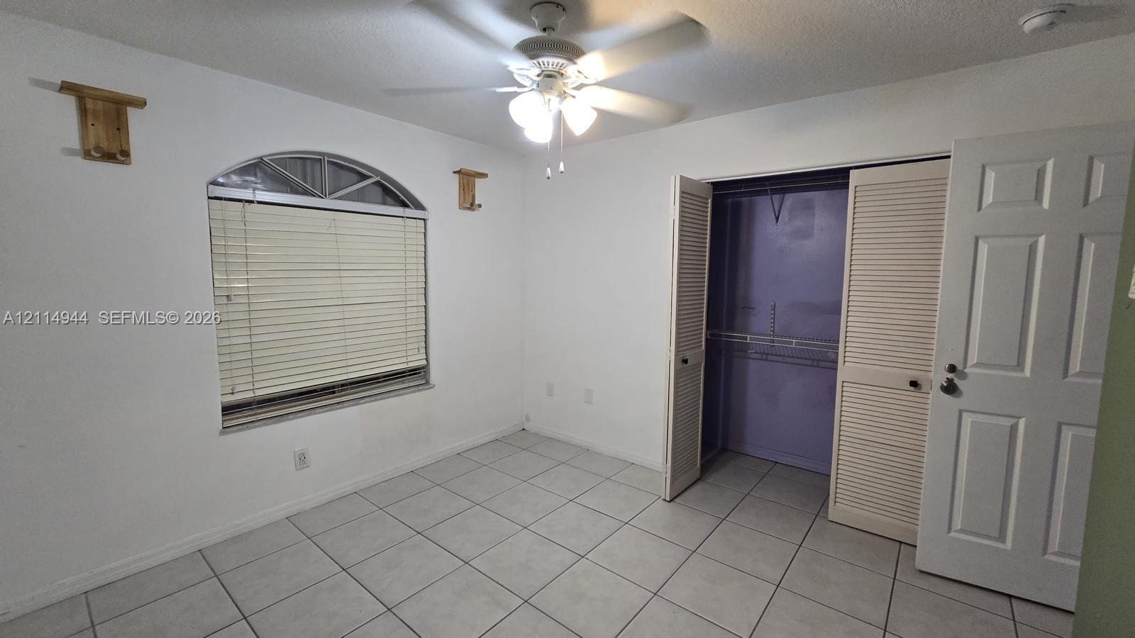 Room featuring arched window, ceramic tile flooring, ceiling fan with integrated lighting, and closet with louvered doors