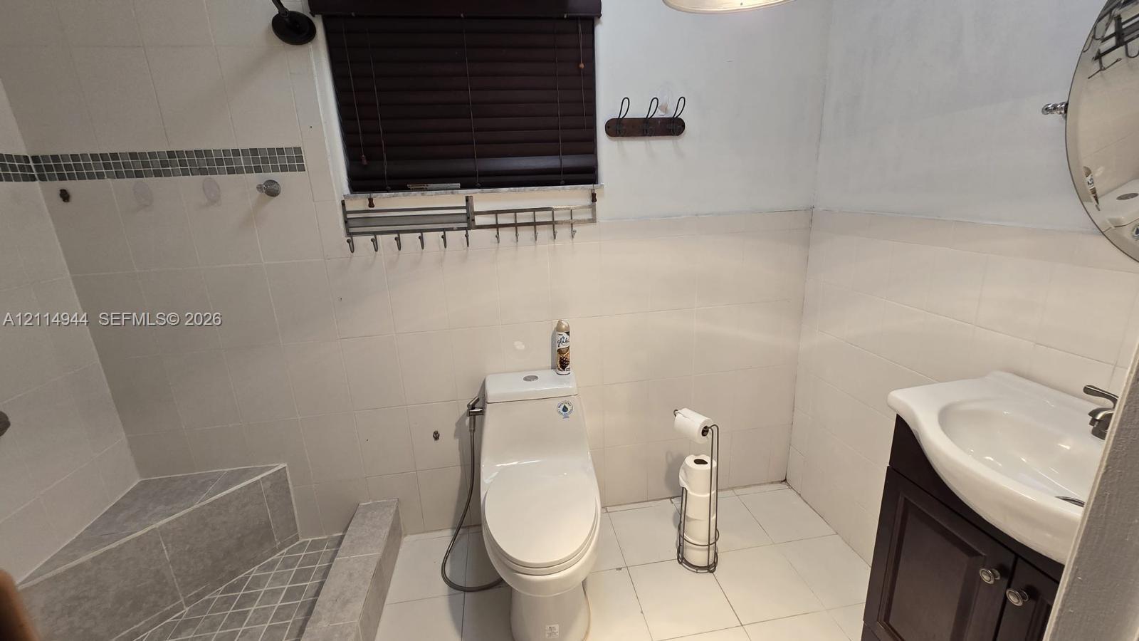 Bathroom featuring white wall tiling with a mosaic accent border, a walk-in tiled shower with a built-in bench, and a dark wood vanity with a white integrated sink