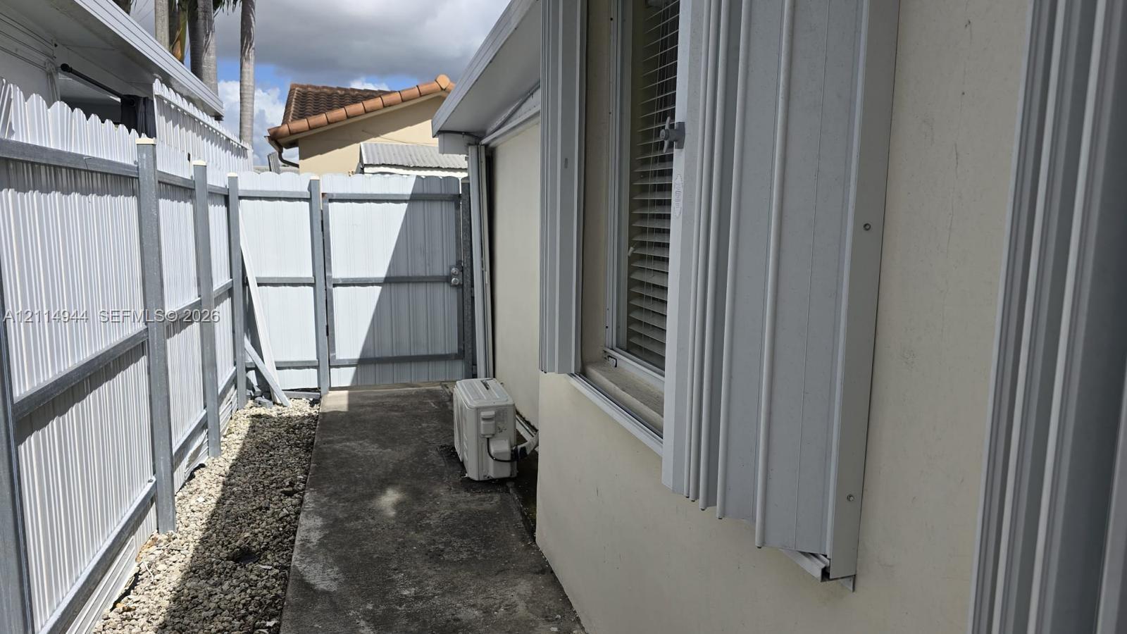 Exterior side area featuring a concrete pathway, tall privacy fencing, and metal accordion-style storm shutters