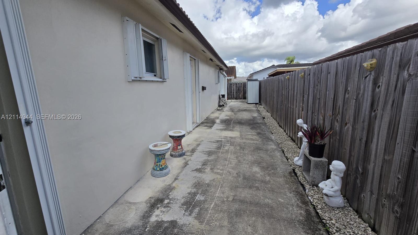 Exterior side yard featuring a concrete pathway, smooth stucco siding, and a wood privacy fence