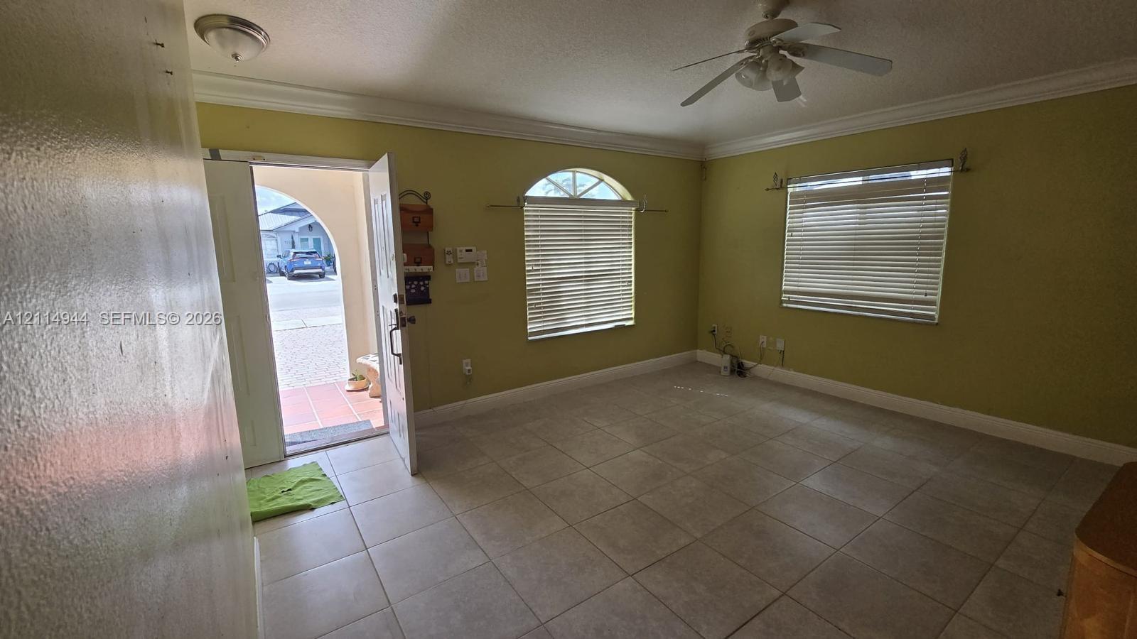 Interior space featuring light-colored tile flooring, crown molding, a ceiling fan, and windows including an arched transom window