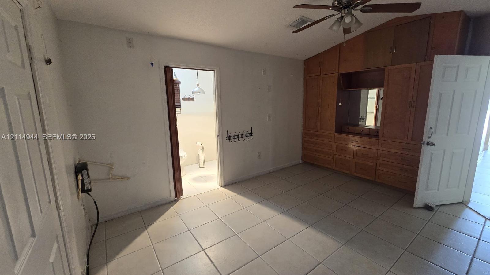 Vaulted ceiling with a central paddle fan, extensive built-in wood-finish cabinetry, and large-format tile flooring