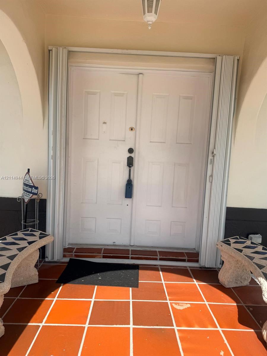 Double entry doors with inset panel detailing, arched covered entryway, and terracotta-style tile flooring