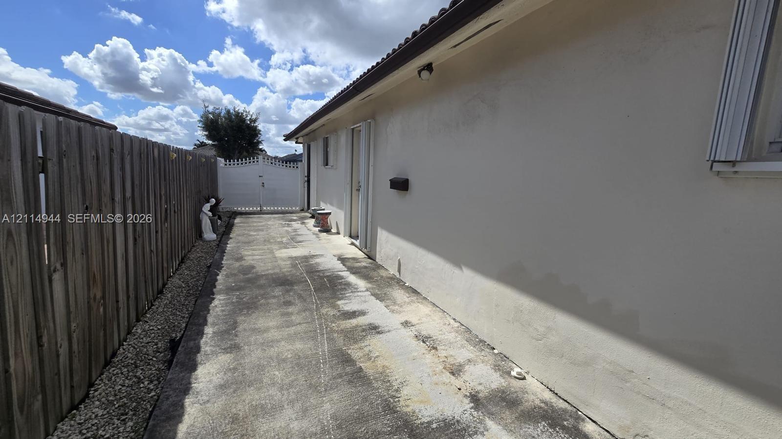 Exterior side yard featuring a concrete pathway, perimeter wood fencing, and a white privacy gate