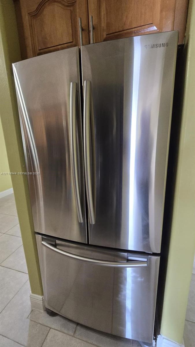 Stainless steel French door refrigerator with bottom-mount freezer, paired with wood-finish cabinetry and tile flooring