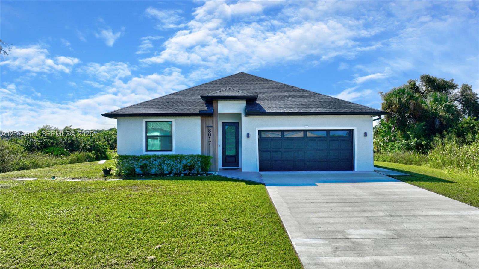 Single-story exterior featuring a light-toned stucco faade, wood-finish entryway accent, attached two-car garage, and a hip roofline