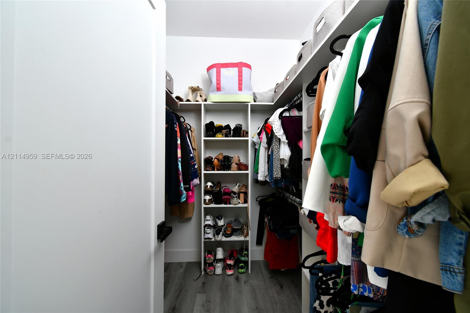 Walk-in closet featuring white built-in shelving, vertical storage tower, and wood-finish flooring