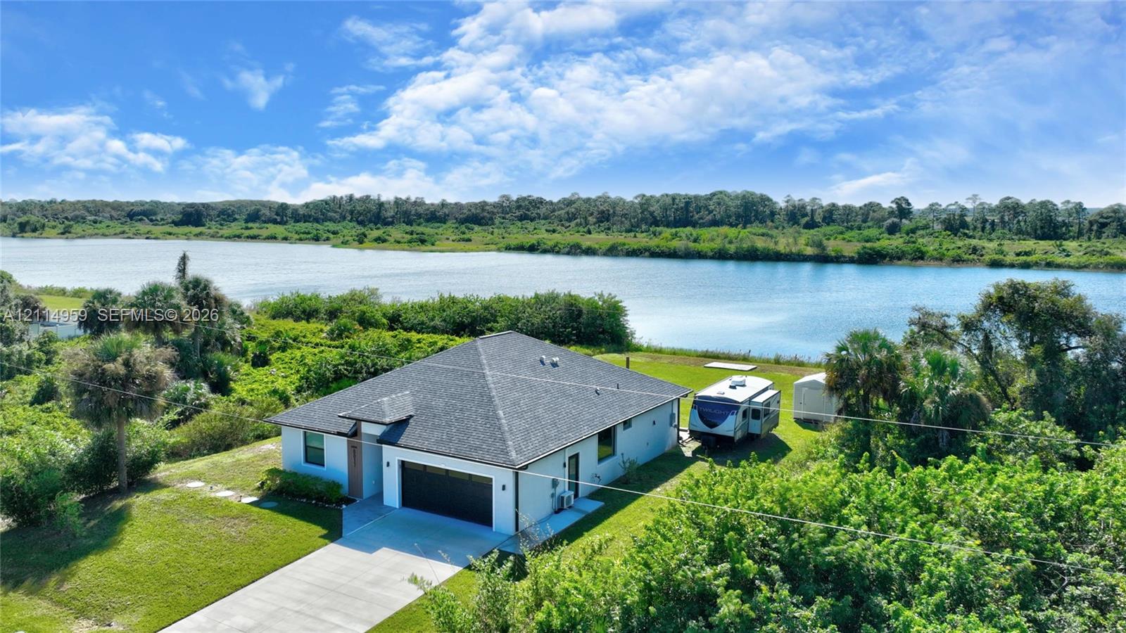 Single-story residence featuring a dark shingle roof, attached two-car garage, concrete driveway, and direct waterfront positioning