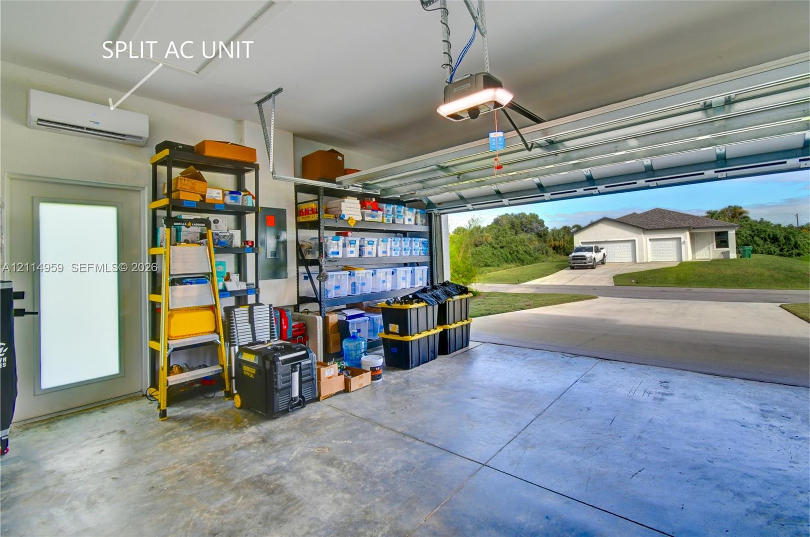 Attached garage featuring concrete flooring, a wall-mounted split-system air conditioning unit, automated garage door opener, and a frosted-glass panel door
