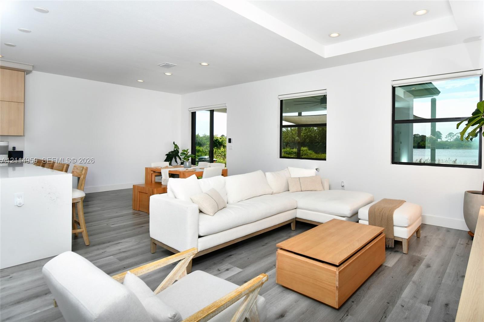 Open-concept living space featuring wood-finish flooring, recessed lighting, a coffered ceiling, a large kitchen island with light-toned surfacing, and black-framed windows