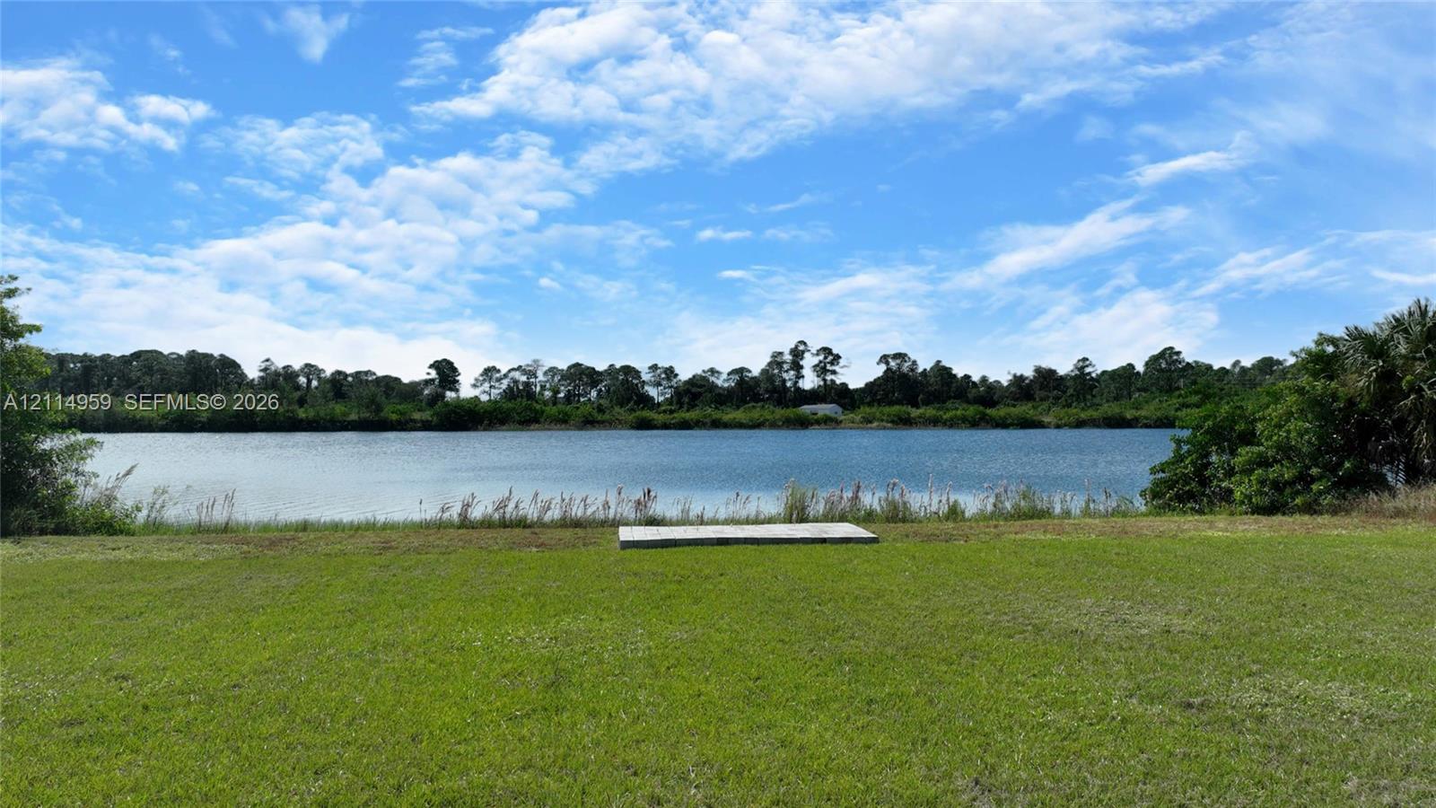 Waterfront lot featuring a manicured lawn, a concrete pad, and mature perimeter trees