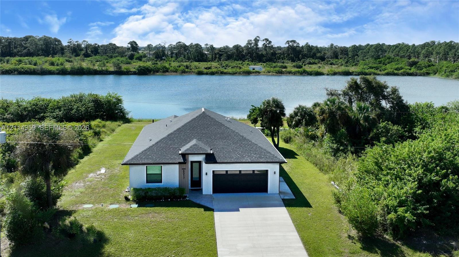Single-story exterior featuring a concrete driveway, two-car garage with modern paneling, hip roofline, and waterfront positioning