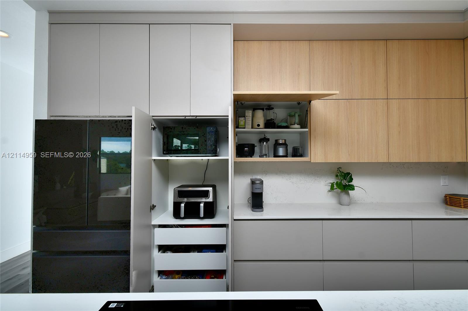 Contemporary kitchen cabinetry featuring matte grey lower drawers, light wood-tone upper cabinets, integrated storage solutions, and white solid-surface countertops