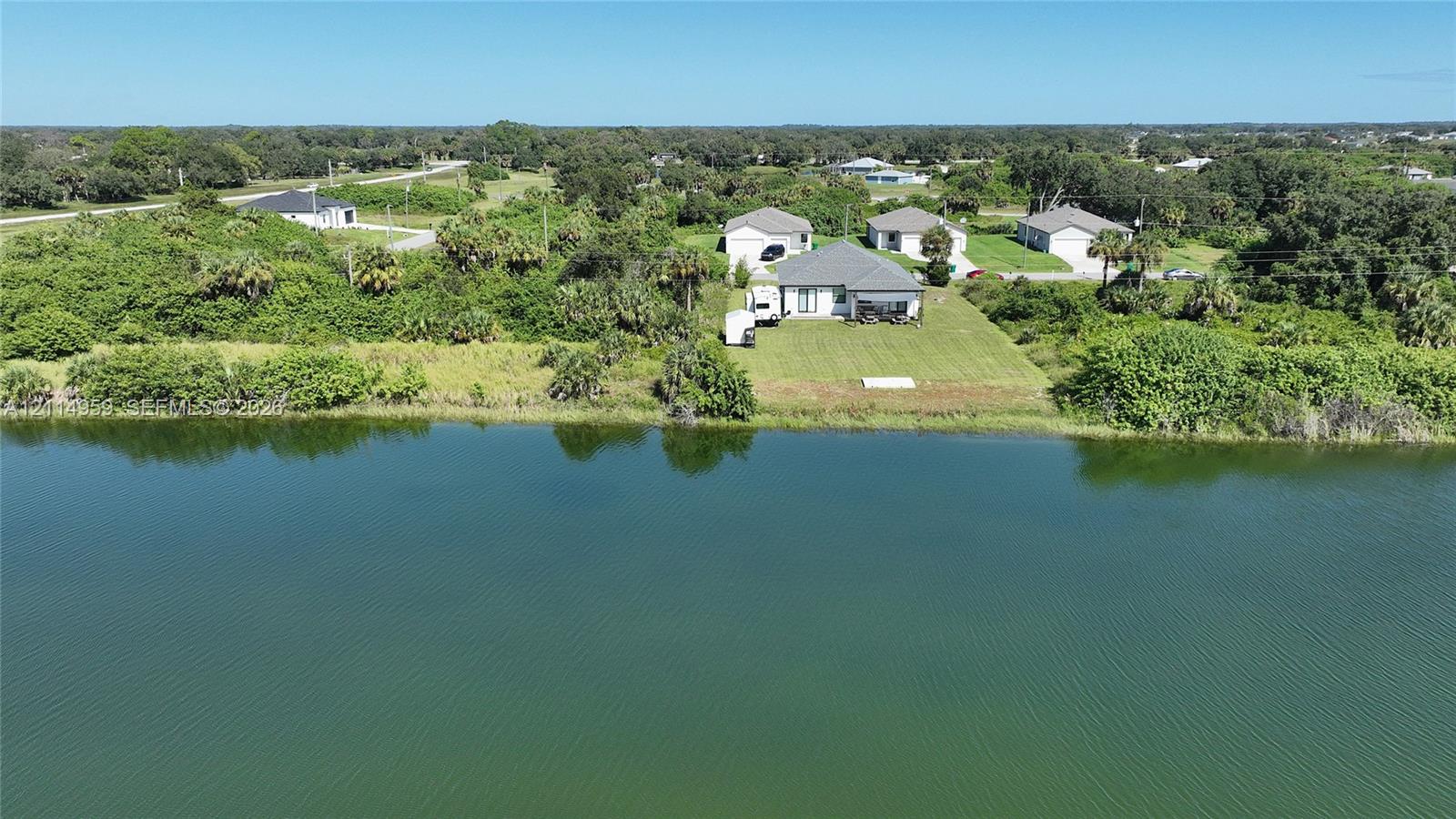 Waterfront property featuring a landscaped lawn, paved driveway, and shingle-roof structure