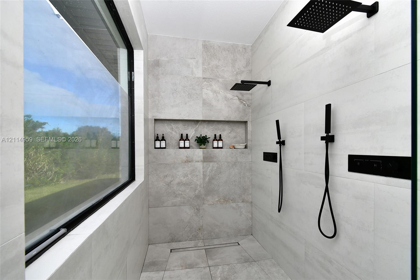 Walk-in shower featuring large-format tile surround, matte black rainfall showerhead, dual handheld sprayers, built-in wall niche, and floor-to-ceiling glass window