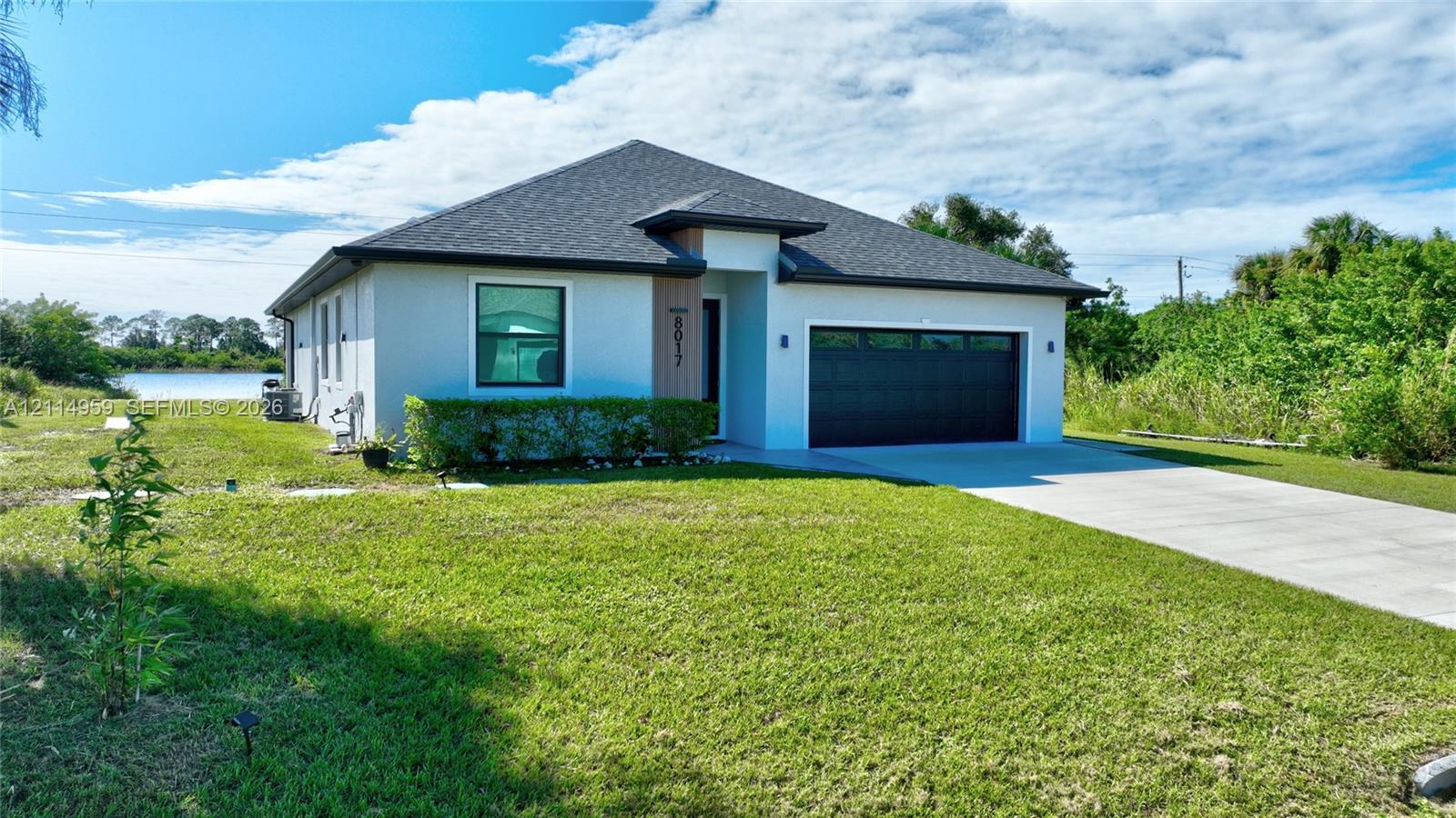 Single-story exterior featuring a hip roof, stucco facade, two-car garage with black sectional door, and water frontage