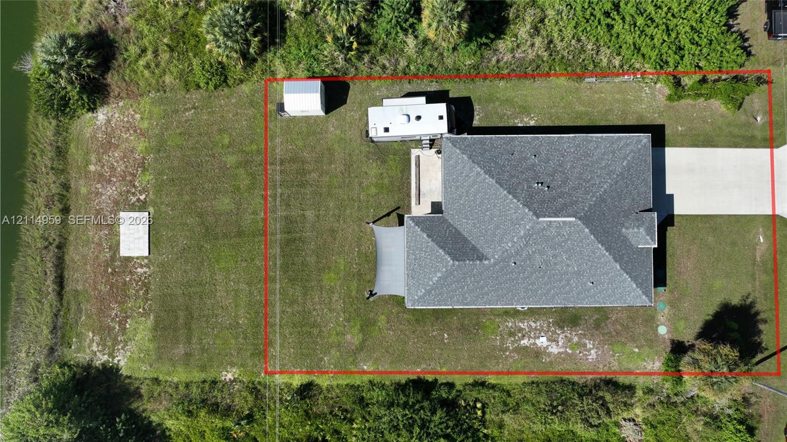 Aerial perspective of the property featuring a concrete driveway, multi-faceted roof structure, detached metal storage building, and grass-covered lot