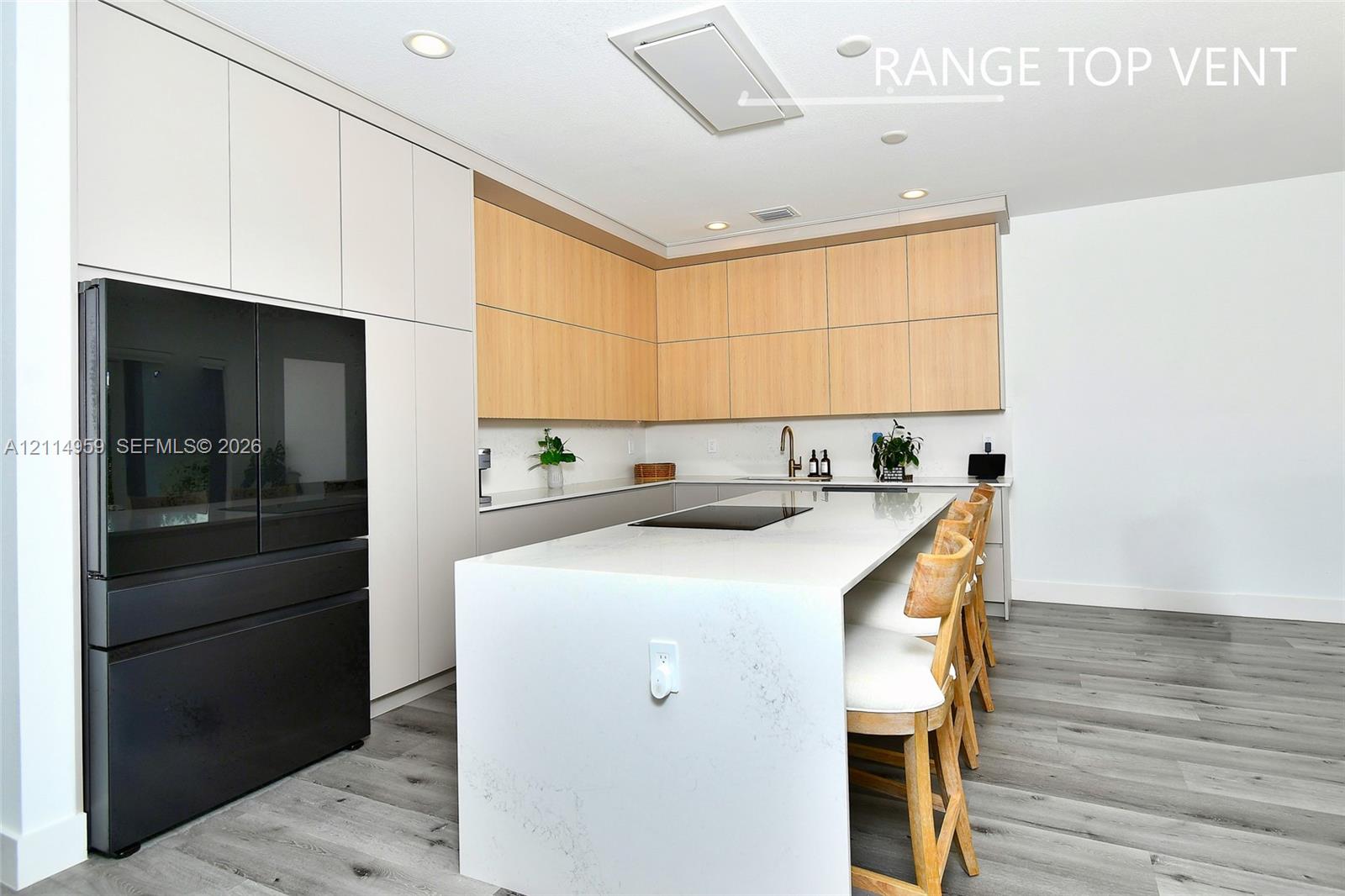 Kitchen featuring slab-style cabinetry in dual finishes, a central island with a solid surface waterfall countertop, integrated cooktop, and wood-finish flooring