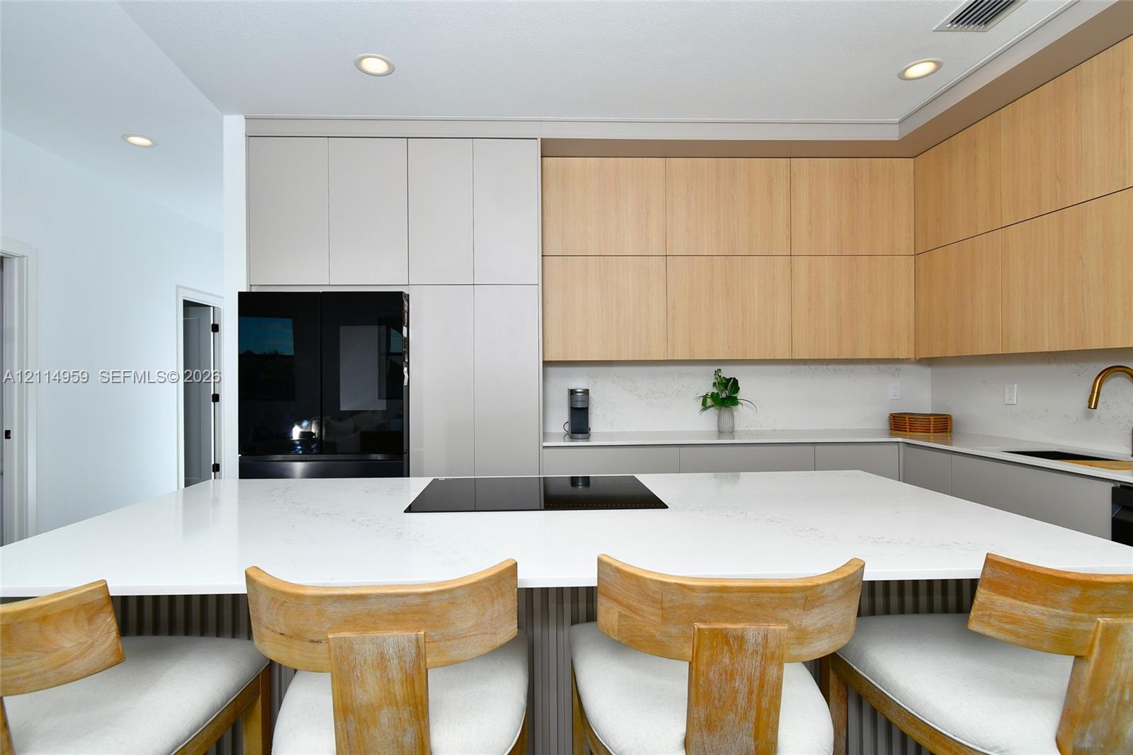 Kitchen featuring a large central island with a stone-finish countertop, flat-panel wood and neutral-toned cabinetry, a built-in black cooktop, and recessed ceiling lighting
