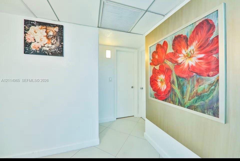 Interior hallway featuring white tile flooring, neutral wall finishes, a wall-mounted light fixture, and panel doors