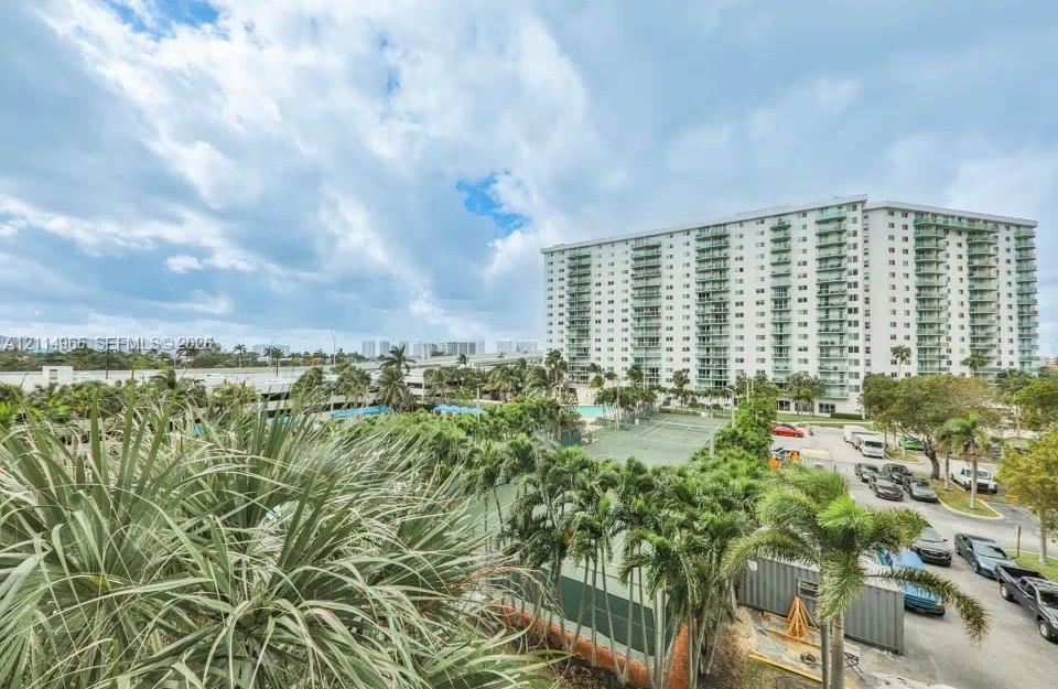 High-rise residential building featuring private balconies, outdoor tennis courts, and mature palm trees