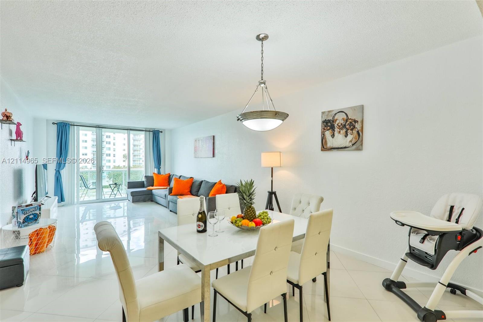 Open-concept living space featuring high-gloss tile flooring, floor-to-ceiling sliding glass doors, and a decorative pendant light fixture