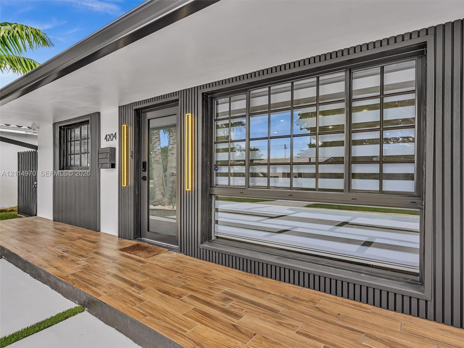 Exterior facade featuring vertical slat siding, wood-finish flooring, full-lite glass entry door, grid-patterned windows, and metallic wall-mounted light fixtures