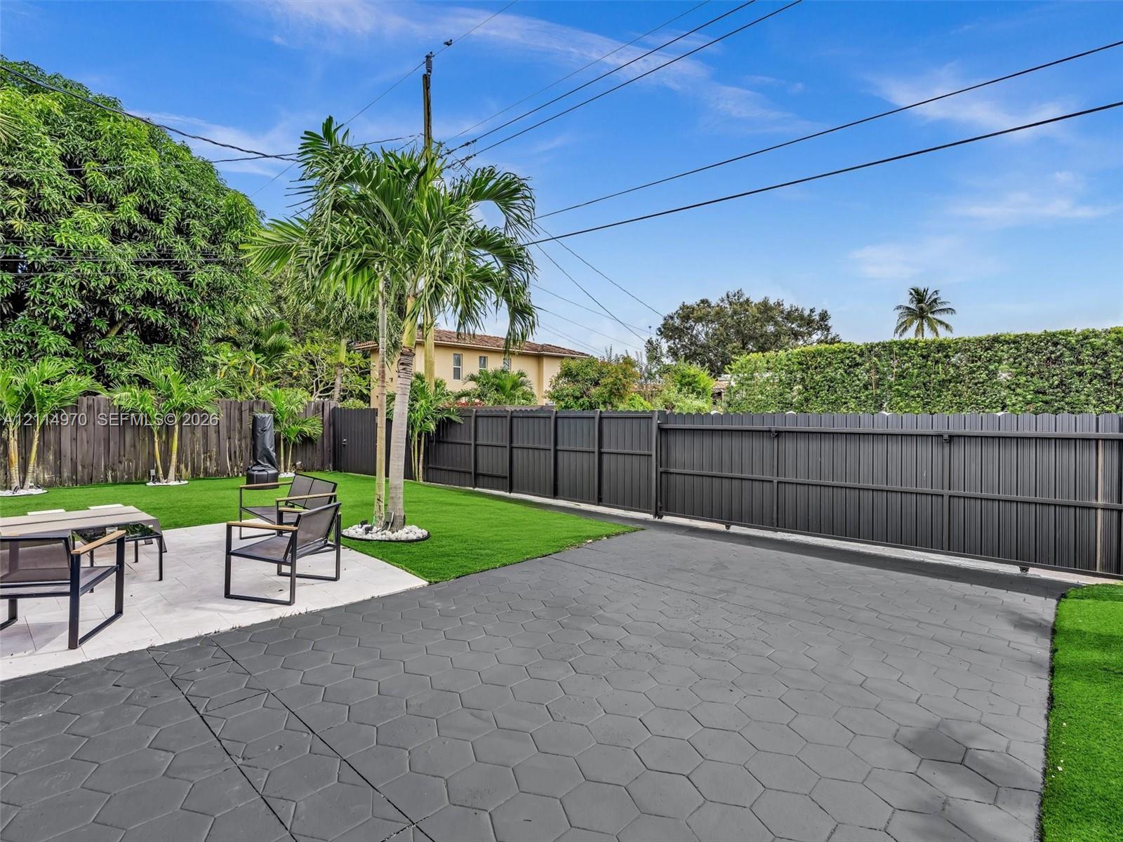 Backyard featuring synthetic turf, a concrete paver patio, a charcoal-toned horizontal slat fence, and mature palm trees